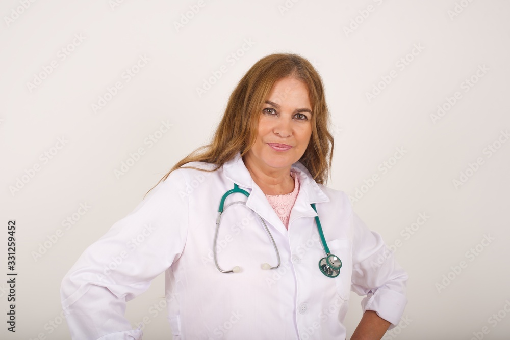 Waist up shot of joyful doctor girl looking up, thinking about something. Hands on hips, doubt facial expression. Standing against gray wall wondering about something happening. Waist up shot of joyful doctor girl looking up, thinking about something. Hands on hips, doubt facial expression. Standing against gray wall wondering about something happening.
