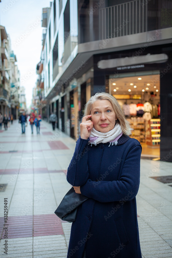 А elderly woman in the street of shops in thought