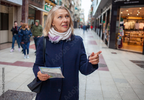 А elderly woman with a map stands on the street of shops