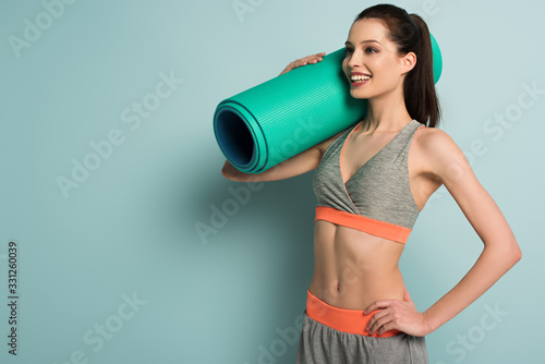 beautiful smiling sportswoman holding fitness mat on blue