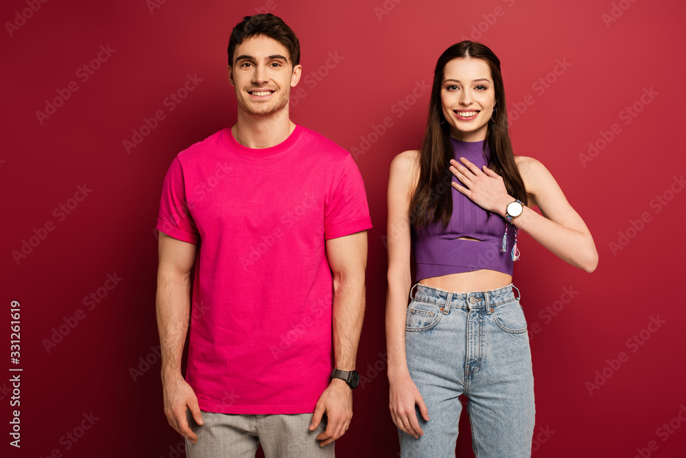 Obraz premium handsome positive man and girlfriend with hand on heart on red