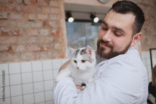 Male veterinarian holding carefully adorable white kitten, working at his clinic