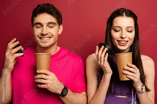 beautiful happy couple smelling coffee in disposable cups on red