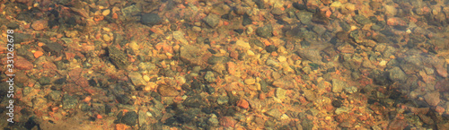 The texture of the river bottom with granite pebbles through the clear spring water. Abstract paints and sketches of nature. Surrealistic palette. Panorama
