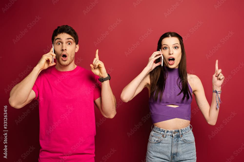 shocked couple talking on smartphones while pointing up on red shocked couple talking on smartphones while pointing up on red