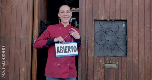 Hispanic woman turning over a sign from closed to open in Spanish