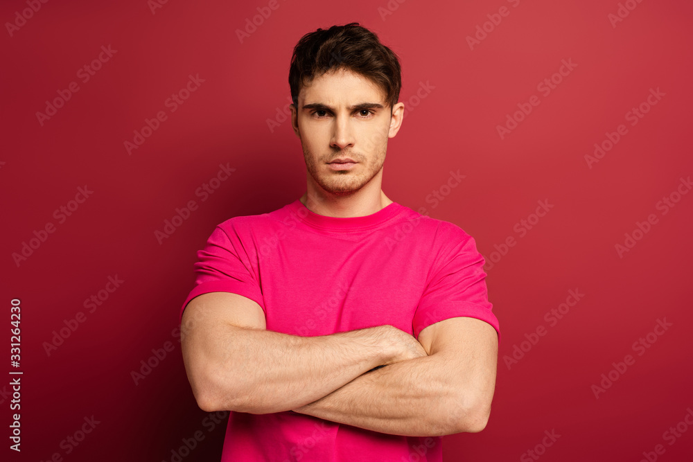 Fototapeta premium portrait of serious man with crossed arms in pink t-shirt on red