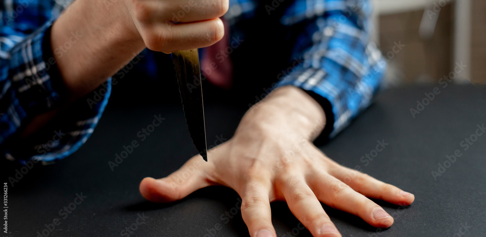 a hand with knife hitting between the fingers on the table, playing the game with a sharp blade wide web banner