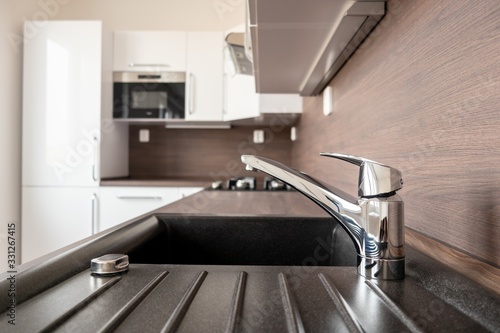 Chrome faucet in a brand new kitchen with blurred background with microwave oven and fridge in a reconstructed home