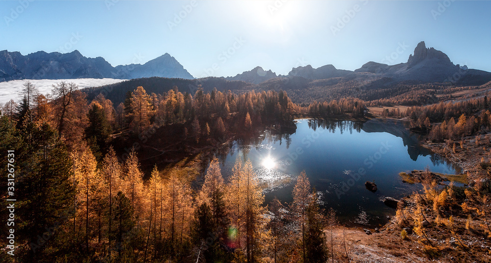 Fototapeta premium Breathtaking aerial views of the crystal clear Lake Federa in Dolomites Alps under sunlight. A magnificent panorama of the mountains. Impressive autumn landscape, with fog during surise. panorama