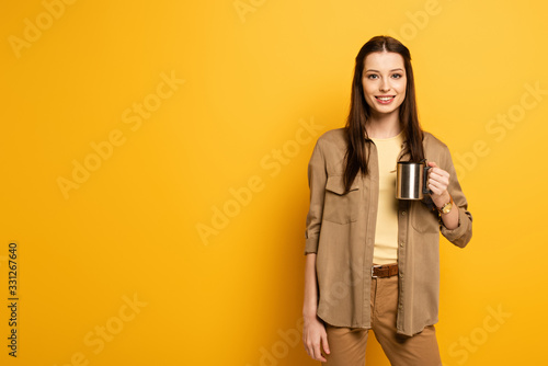 beautiful smiling female traveler holding coffee cup on yellow