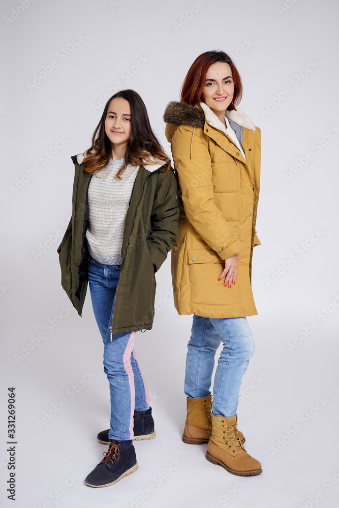 portrait of smiling mother and daughter in warm clothes posing over grey portrait of smiling mother and daughter in warm clothes posing over grey