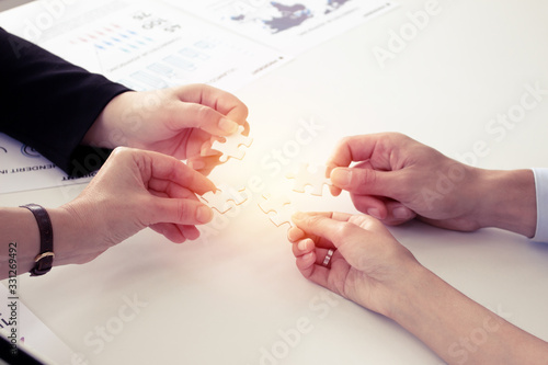 Closeup of businesspeople holding jigsaw puzzle.