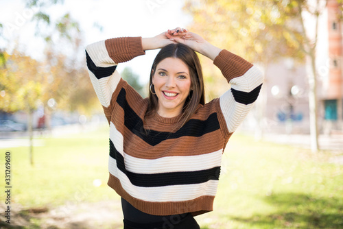 Portrait of beautiful brunette female looks with excitement at camera, keeps hands raised over head notices something unexpected, isolated over gray wall. Lovely woman reacts on sudden news.