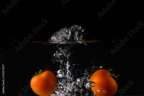 Isolated Tomatos splashing into water on a black background creating bubbles