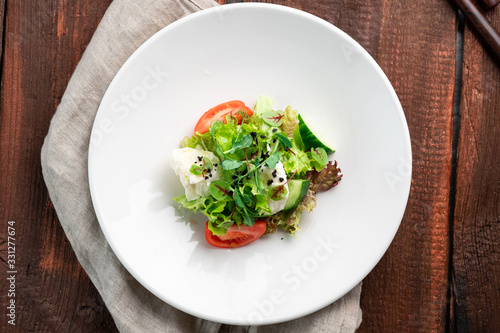 Light diet salad of mozzarella and fresh vegetables -cucumber, tomato, lettuce, peas on a white plate on a wooden background
