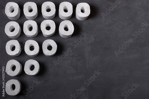 Many toilet paper rolls on dark concrete background. White toilet paper. Top view. Copy space.