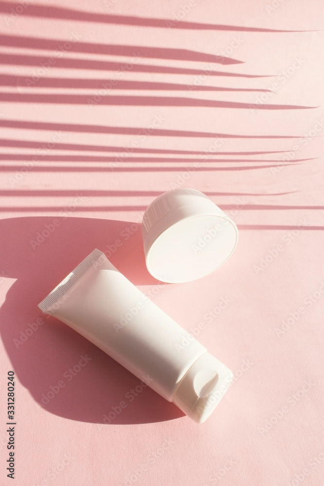 Fototapeta premium A tube of cosmetics with a shadow from a palm leaf. The concept of minimalism cosmetic packaging. Layout for branding, labels and packaging.