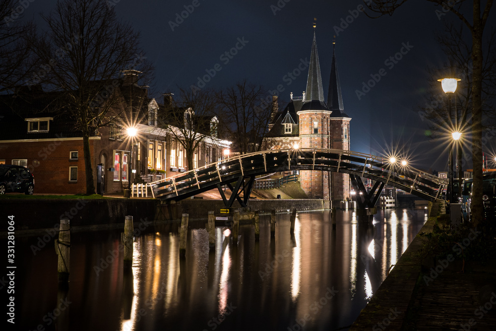 Fototapeta premium The famous historical 'Waterpoort' in the city of Sneek at night with old typical frisian wooden canal bridge - Sneek, Friesland, The Netherlands