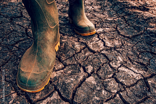 Farmer in rubber boots walking on dry soil ground