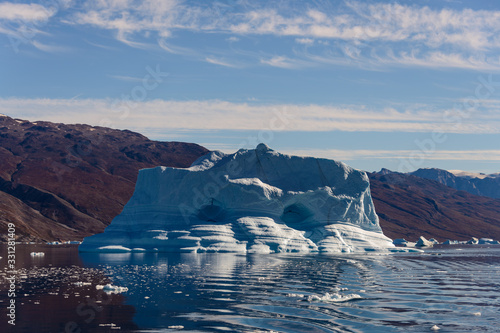 Iceberg in Greenland fjord with reflection in calm water. Sunny weather. Golden hour.