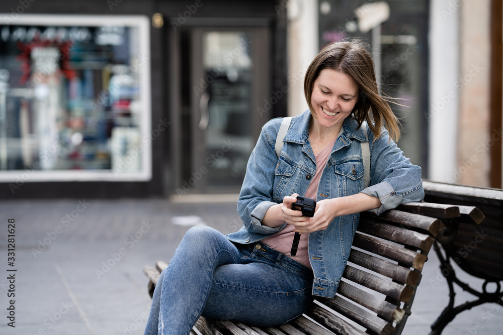 smiling girl sitting on a bench on the street examining her action camera