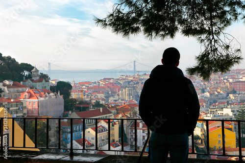 A young man watching the beautiful morning panorama of Lisbon from the famous Miradouro da Graca viewpoint, Portugal