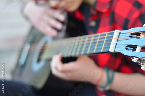 The neck of a classic black guitar. The girl's fingers pluck the strings. Songs with a guitar in the yard. Selective focus, close-up, background blur.