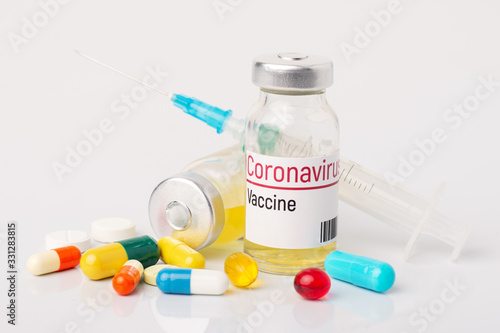 Ampule with coronavirus vaccine and many pills on white table. Discovering vaccine against coronavirus