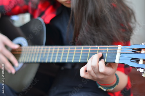 The neck of a classic black guitar. The girl's fingers pluck the strings. Songs with a guitar in the yard. Selective focus, close-up, background blur.