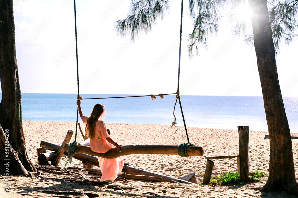 young woman sitting alone on wooden swing wiggle around on the sea beach of the island, quiet and private silent place far away island