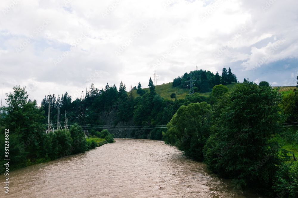 Carpathian mountain river in clouny day. Grey and fast water in little stream.Ukrainian village in overcast day. Country side view of cloudy vertex in the middle of summer. Nobody. Season of rain. 