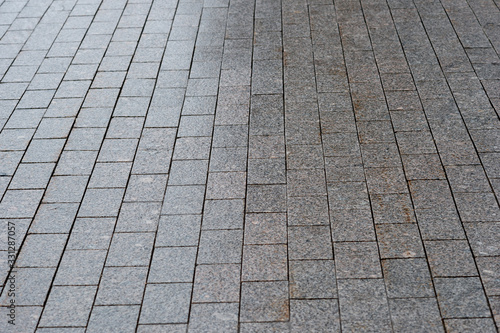 The sidewalk is paved with granite with uneven lighting gradient. Background