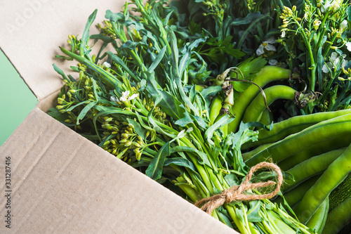 Green produce vegetables and herbs in cardboard box. Healthy organic food delivery concept