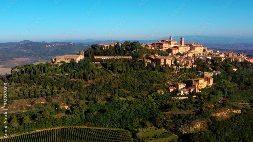 Drone flying over a magnificent authentic Italian cityscape and green meadows. Aerial view of the beautiful medieval old town of Montepulciano with red roofs Tuscany, Italy