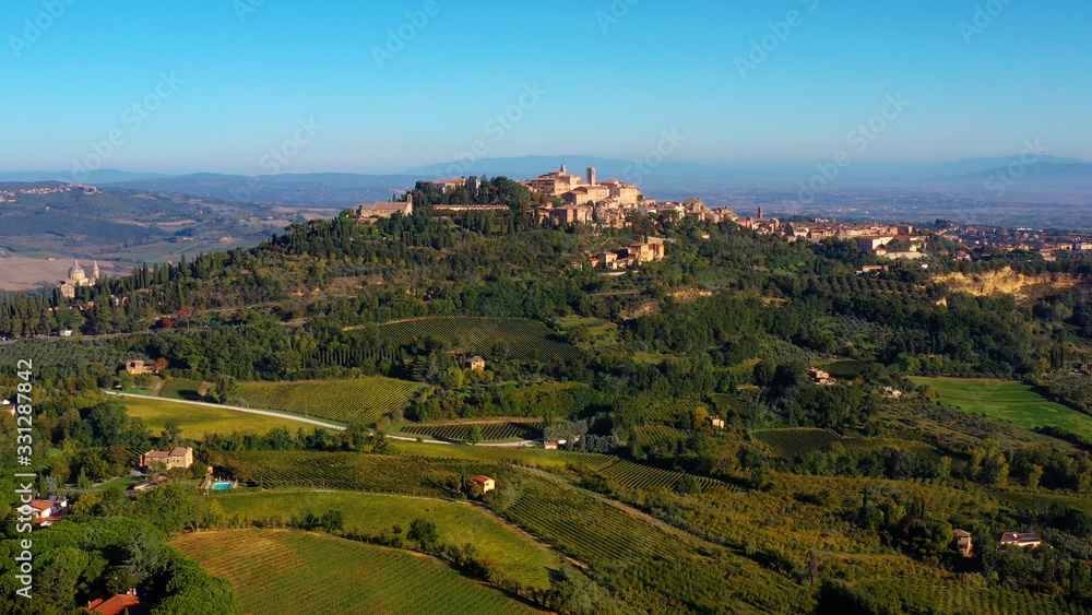 Obraz premium Drone flying over a magnificent authentic Italian cityscape and green meadows. Aerial view of the beautiful medieval old town of Montepulciano with red roofs Tuscany, Italy