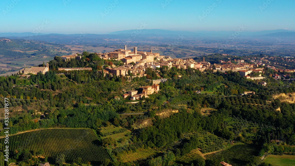 Fototapeta premium Drone flying over a magnificent authentic Italian cityscape and green meadows. Aerial view of the beautiful medieval old town of Montepulciano with red roofs Tuscany, Italy