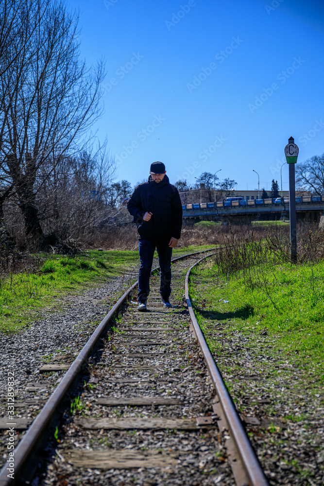 Cheerful attractive bearded young man with backpack walking along railroad.
