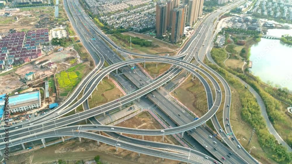 Top view to the cars driving on multi-level highway on the sunset. Highway multilevel junction road passing through the chinese city center. Highway overpass and junction with cars, trucks and buses. Top view to the cars driving on multi-level highway on the sunset. Highway multilevel junction road passing through the chinese city center. Highway overpass and junction with cars, trucks and buses.