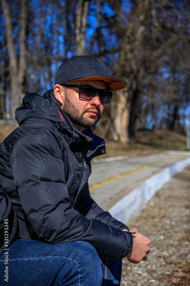 custom made wallpaper toronto digitalStylish young man with a cap, sunglasses, sneakers in a denim jacket with a backpack sits on golden foliage in the park. Attractive hipster guy is rests at the forest.
