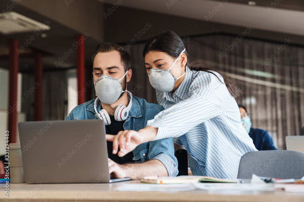 Photo of young students in medical masks studying with laptop Photo of young students in medical masks studying with laptop