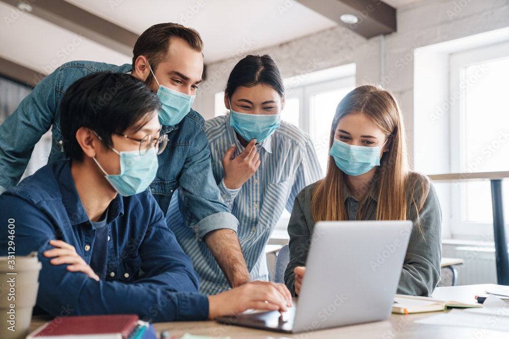 Photo of pleased students in medical masks studying with laptop Photo of pleased students in medical masks studying with laptop