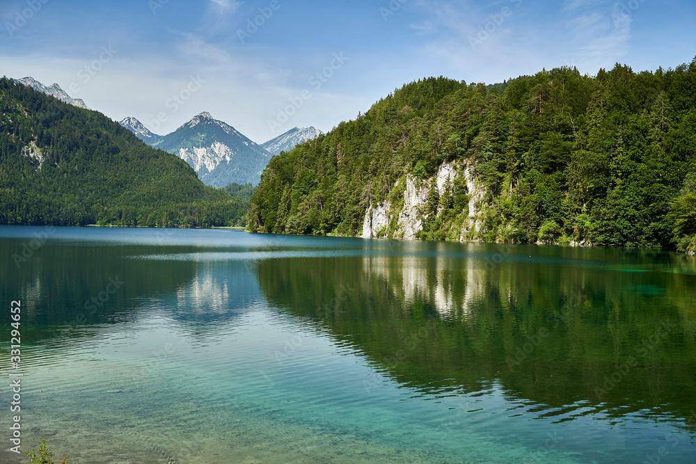 Alpsee lake near Hoehenschwangau and Neuschwanstein castle in Bavaria, Germany. A clear summer sky and Alps in the background.