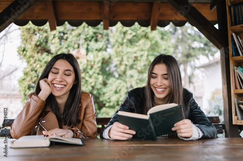 Two smiling girls sitting in pavilion with books