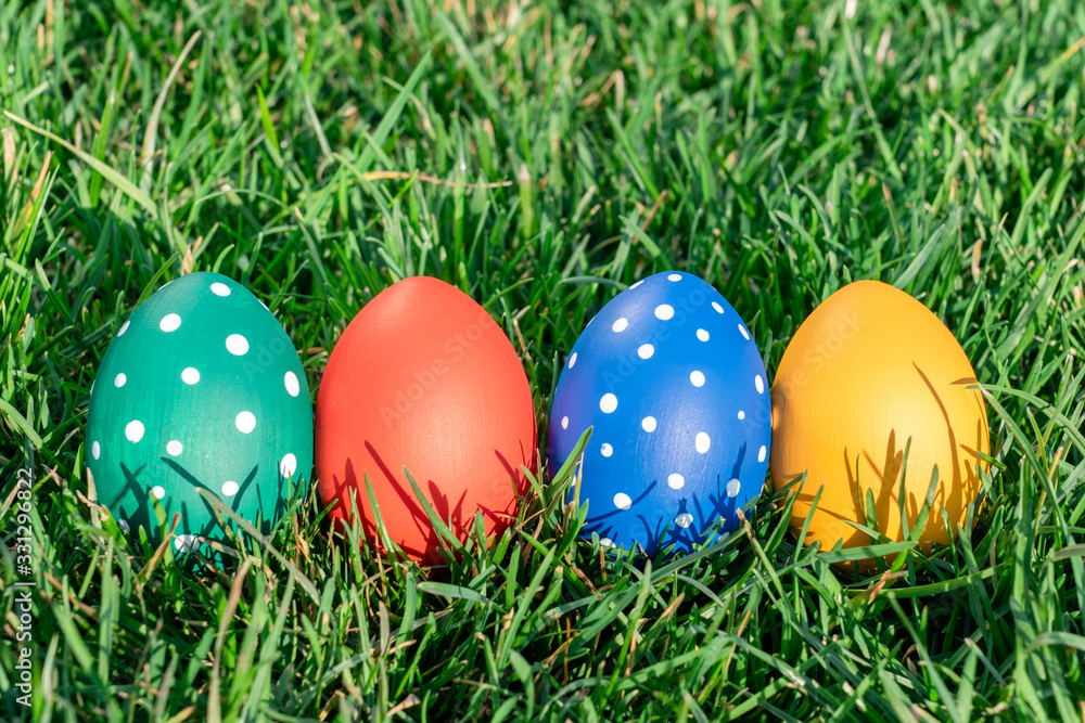 four easter eggs of different colors lay on green spring grass, space for text, celebration of easter holiday, geetings concept
