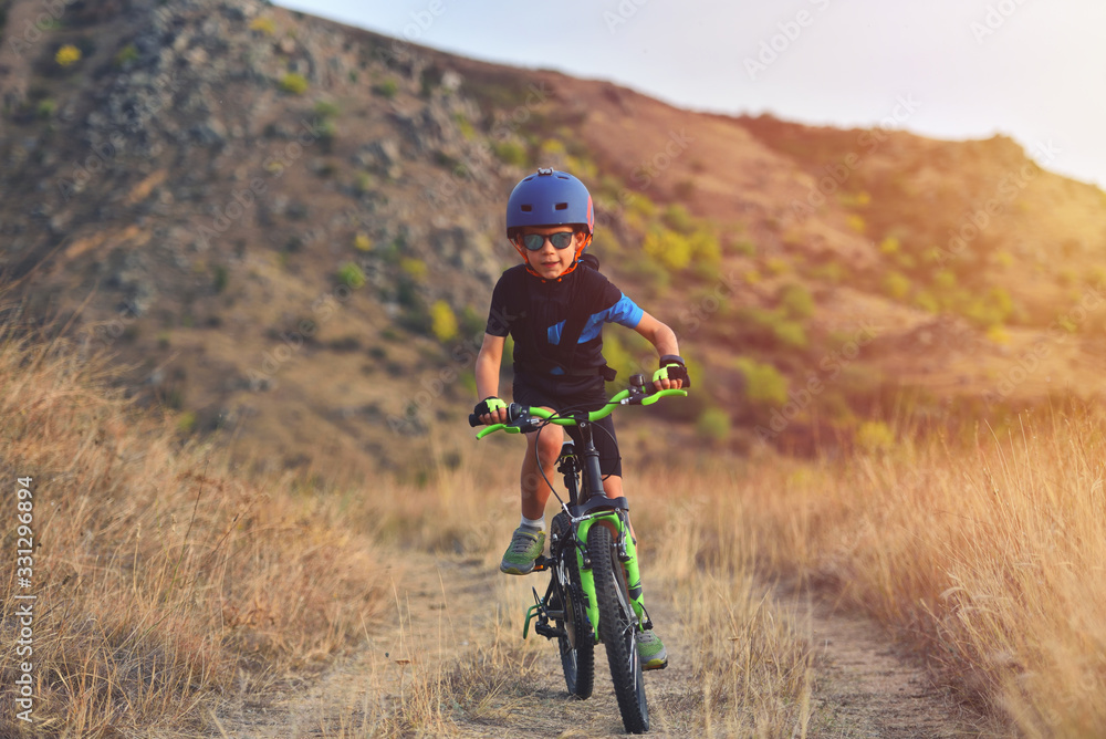 Happy kid boy of 7 years having fun in autumn park with a bicycle on beautiful fall day. Active child wearing bike helmet