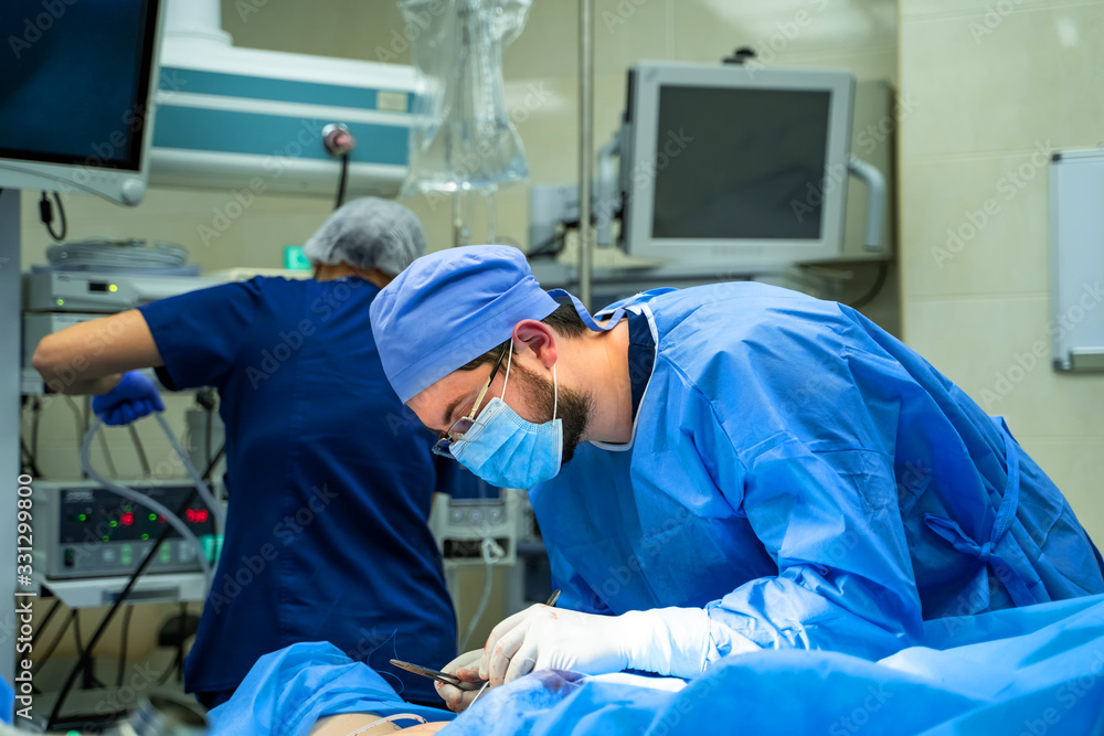 Group of doctors perform an operation to a patient. Surgeons in medical uniform and masks working in the operating room Group of doctors perform an operation to a patient. Surgeons in medical uniform and masks working in the operating room