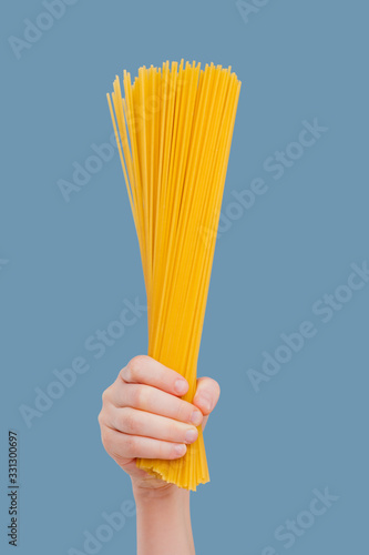 close up, child hand holding raw spaghetti isolated on blue background