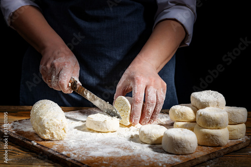 Female hands knead the dough on a wooden antique table on a dark background, close-up, shallow depth of field, beautiful directional lighting. Concept of home baking and comfort.