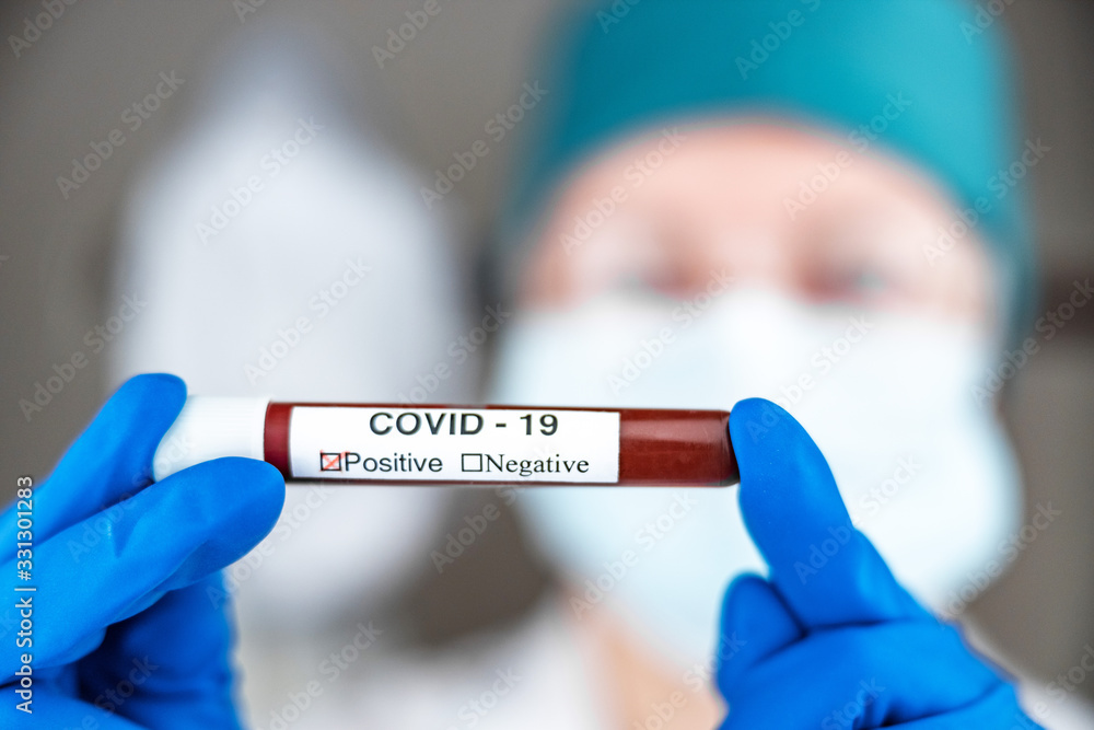 A nurse in a respiratory mask holds a test tube labeled COVID 19, with a positive blood test for a new rapidly spreading coronavirus, close-up, shallow depth of field, selective focus. The concept of A nurse in a respiratory mask holds a test tube labeled COVID 19, with a positive blood test for a new rapidly spreading coronavirus, close-up, shallow depth of field, selective focus. The concept of